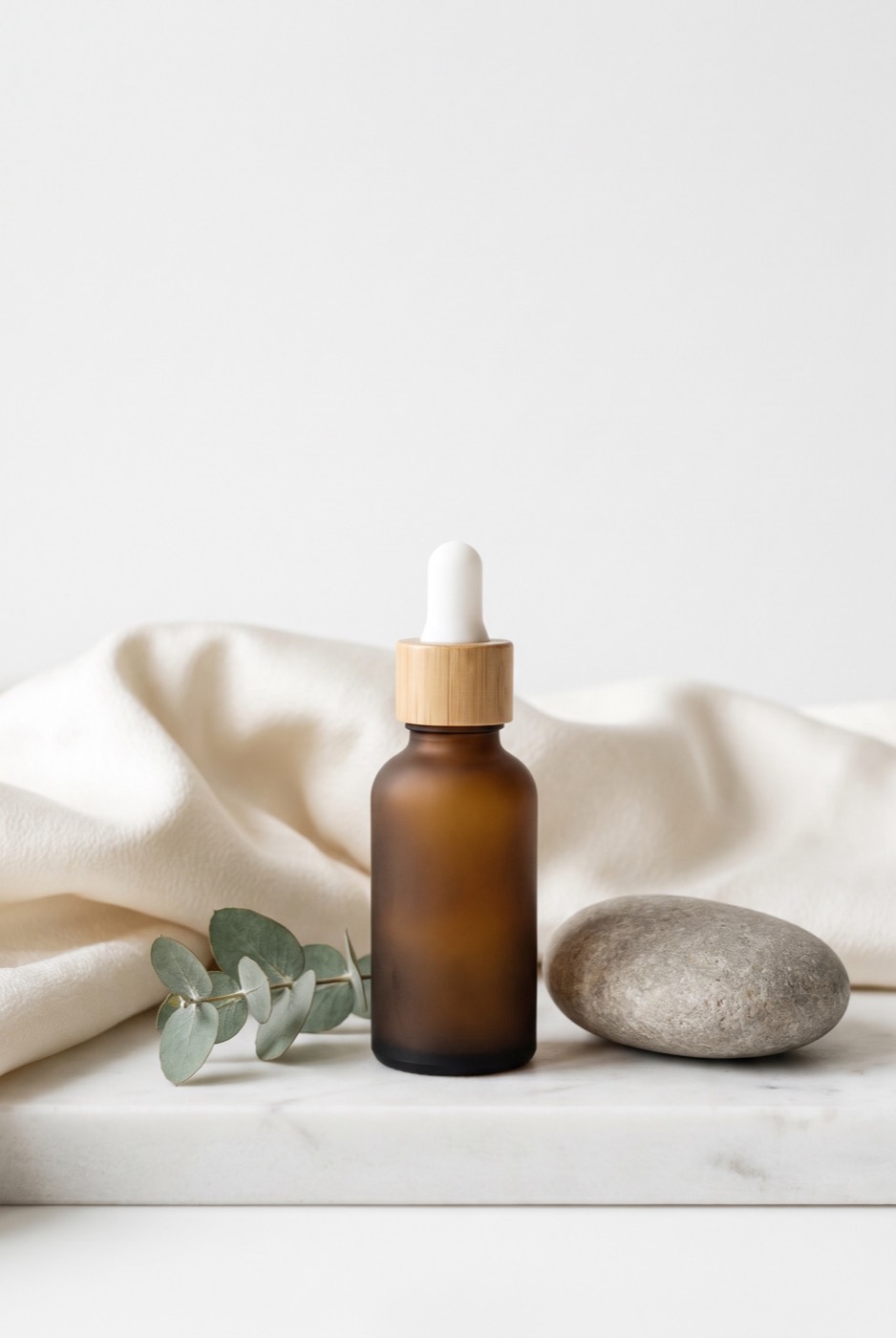 A bottle, a sprig of eucalyptus and a river stone on marble