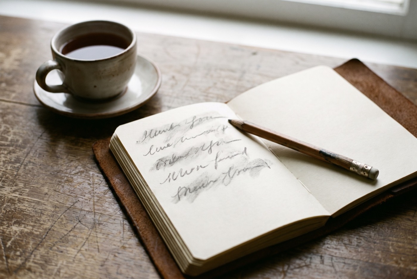 An open notebook with five short pencil lines, a pencil and a cup of tea