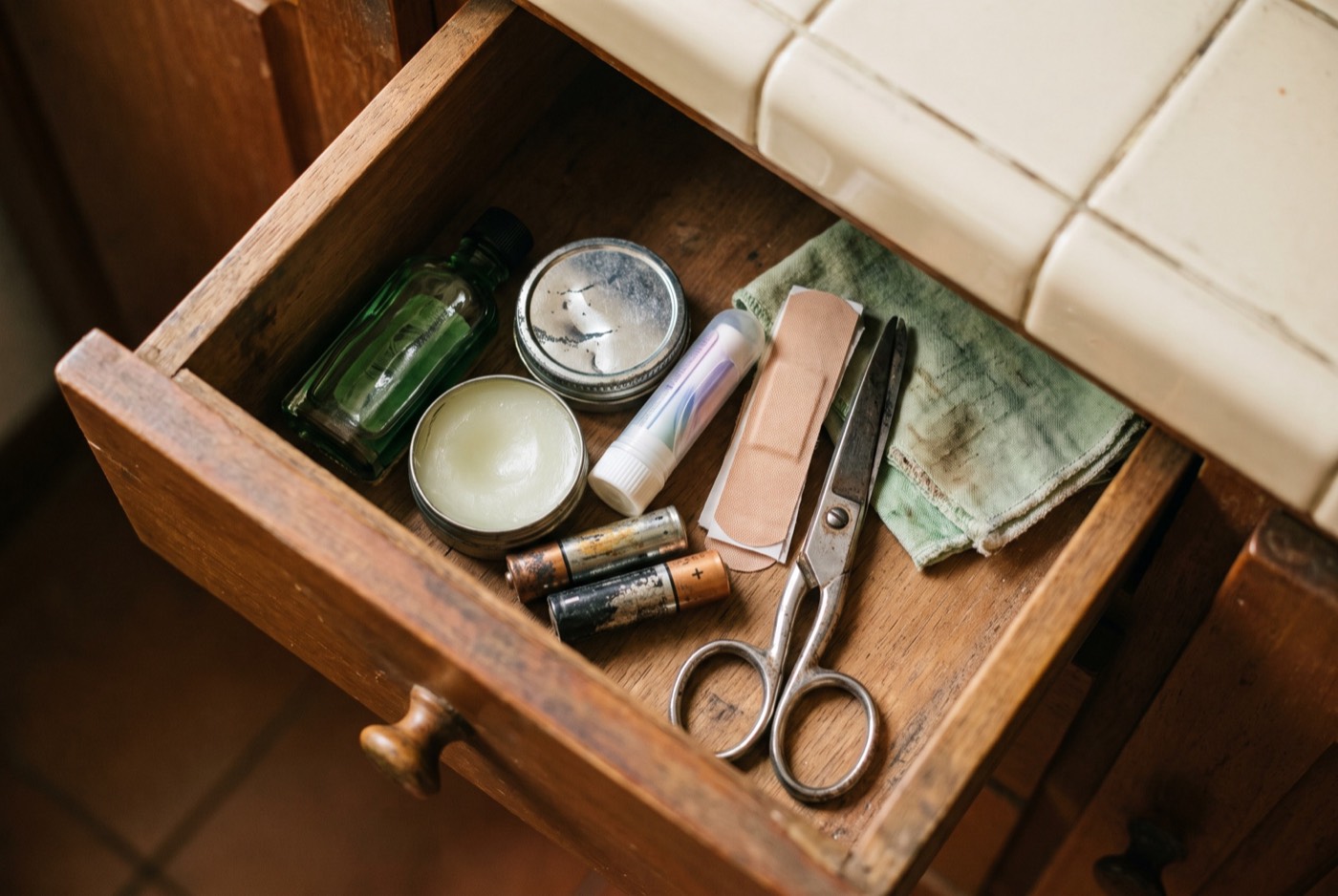 A kitchen drawer with medicated oil, a tin of balm, an inhaler, plasters and batteries